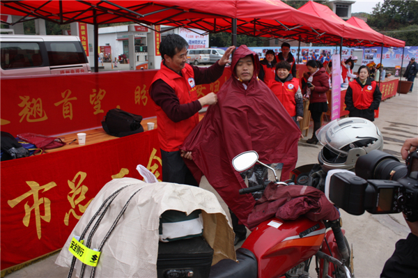 梧州市總工會的黨員義工們在市東出口春運服務(wù)站助力“摩托大軍”平安返鄉(xiāng)，幫助他們檢查車輛和行李，穿上雨衣。--黃賀峰攝.j